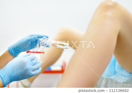 Gynecologist examines a patient laying on gynecological chair using medical vaginal speculum. Doctor takes a smear from a young woman cervix. Diagnosis of diseases. 112136682