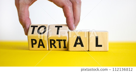 Total or partial symbol. Businessman turns beautiful wooden cubes and changes the word Partial to Total. Beautiful yellow table white background. Business and total or partial concept. Copy space. 112136812
