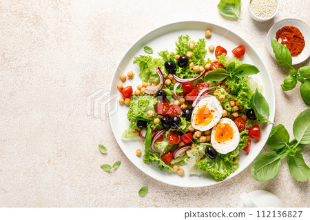 Soft-boiled egg Easter fresh vegetable salad with tomatoes, chickpea, olives, onion and green lettuce. Healthy food, breakfast. Top view 112136827