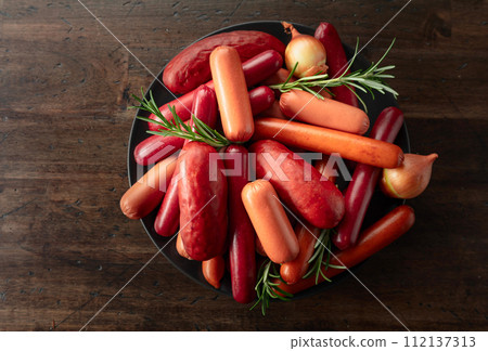 Various sausages with rosemary and onion on a old wooden table. 112137313