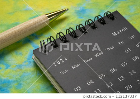March 2024 - small spiral desktop calendar with a stylish pen against colorful marbled paper, time and business concept 112137337
