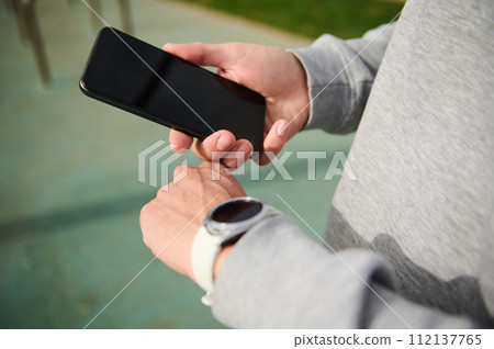 Close-up hands of a runner checking timer, clock and healthy training progress with smart wrist watch and mobile phone 112137765