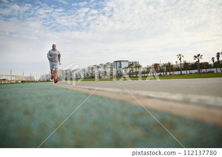 Full length portrait. Bottom view. Determined man athlete running in the city during morning cardio workout. Full length portrait. Bottom view. Determined man athlete running in the city during morning cardio workout. 112137780