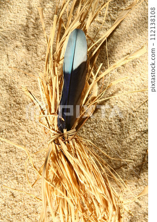 A feather is tied to a bundle of straw on a sandy beach 112138108