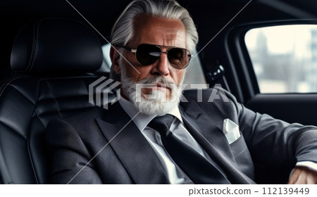 Senior businessman with grey hair and beard exuding confidence, sitting in luxurious black car 112139449