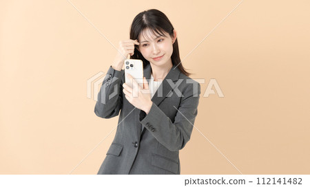 一位女士一邊看著智慧型手機螢幕一邊檢查自己的妝容 112141482