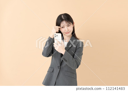 一位女士一邊看著智慧型手機螢幕一邊檢查自己的妝容 一位女士一邊看著智慧型手機螢幕一邊檢查自己的妝容 112141483