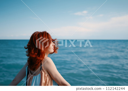 Captured against the vibrant blue sea, a young woman on the beach turns her head to look over her shoulder. Captured against the vibrant blue sea, a young woman on the beach turns her head to look over her shoulder. 112142244
