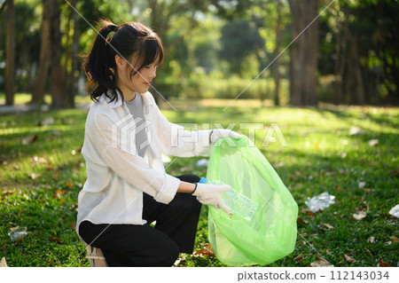 Smiling young woman collecting plastic bottles in the park. Environmental responsibility concept Smiling young woman collecting plastic bottles in the park. Environmental responsibility concept 112143034