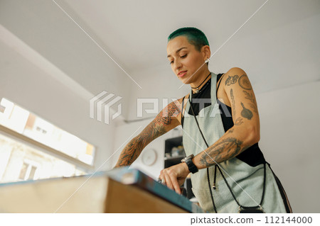 Woman with squeegee is pressing ink on frame working in design studio. Silk screen printing 112144000
