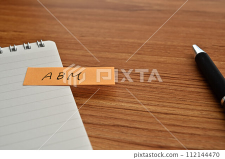 A sticky note with ABM written on it, a notebook, and a pen 112144470