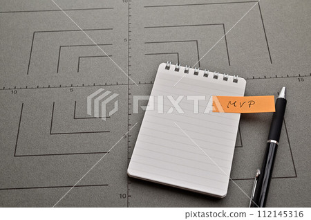一張寫有 MVP 的便利貼,寫在灰色圖表、筆記本和筆上 一張寫有 MVP 的便利貼,寫在灰色圖表、筆記本和筆上 112145316