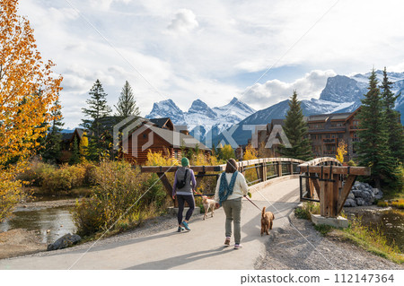 Residents walking the dogs in Town of Canmore in fall season. Canmore Opera House at Spring Creek beside the wooden boardwalk bridge. Alberta, Canada. Residents walking the dogs in Town of Canmore in fall season. Canmore Opera House at Spring Creek beside the wooden boardwalk bridge. Alberta, Canada. 112147364