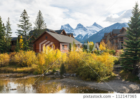 Town of Canmore in autumn. Alberta, Canada. Canmore Opera House at Spring Creek. The Three Sisters trio of peaks in the background. Town of Canmore in autumn. Alberta, Canada. Canmore Opera House at Spring Creek. The Three Sisters trio of peaks in the background. 112147365