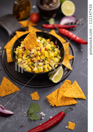 Freshly made mango salsa in a black ceramic bowl and nacho chips 112147438