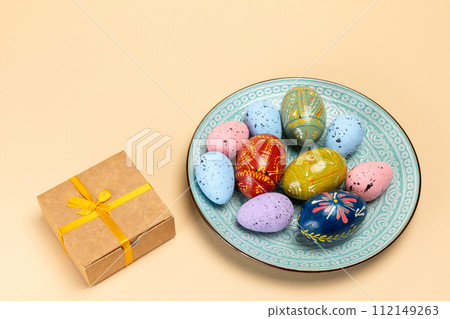 Dish with colored Easter eggs and a gift box. Dish with colored Easter eggs and a gift box. 112149263