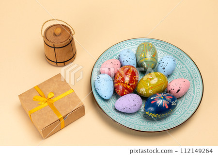 Dish with colored Easter eggs and a gift box. Dish with colored Easter eggs and a gift box. 112149264