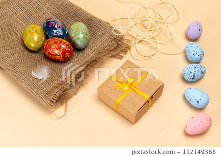 Easter eggs on a sackcloth bag and a gift box on the beige background. Easter eggs on a sackcloth bag and a gift box on the beige background. 112149368