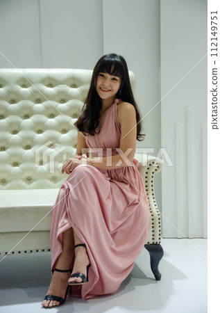 asian young girl is wearing pink dress is sitting on luxury white sofa in studio asian young girl is wearing pink dress is sitting on luxury white sofa in studio 112149751