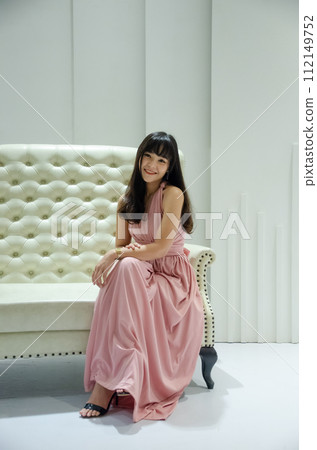 asian young girl is wearing pink dress is sitting on luxury white sofa in studio asian young girl is wearing pink dress is sitting on luxury white sofa in studio 112149752