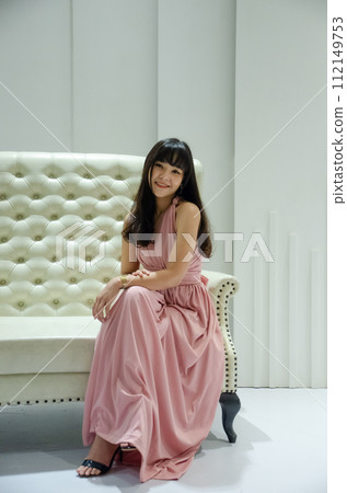 asian young girl is wearing pink dress is sitting on luxury white sofa in studio asian young girl is wearing pink dress is sitting on luxury white sofa in studio 112149753