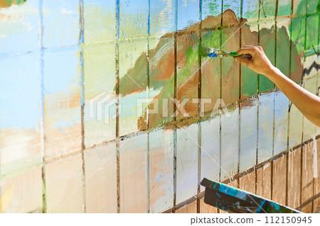 Female artist's hand with a brush painting on the wall with different colors Female artist's hand with a brush painting on the wall with different colors 112150945