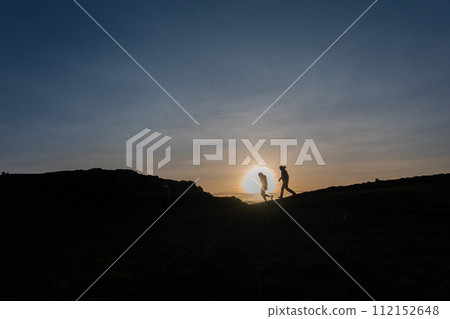 Person watching sunset in a field, standing on a hill, surrounded by nature's beauty Person watching sunset in a field, standing on a hill, surrounded by nature's beauty 112152648
