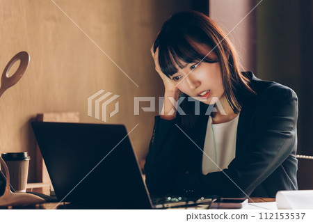 A worried businesswoman holding her head while using a computer 112153537