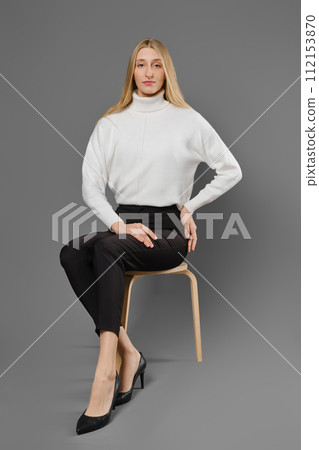 Long-legged young woman woman in trousers and sweater sitting on a chair in a beautiful pose 112153870