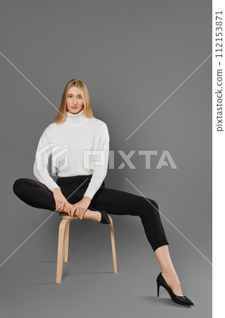 Long-legged woman woman in trousers and sweater sitting on a chair in a fashionable pose 112153871