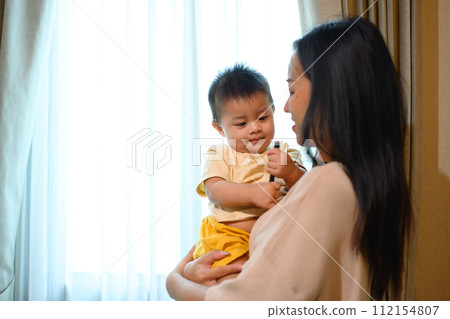Happy young mom with cute little baby son standing in bedroom. Family, motherhood and child care concept 112154807