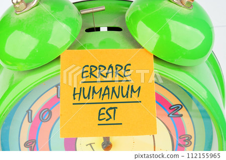 Latin quote Errare humanum est, meaning It is human nature to make mistakes. Mistakes are inherent in human existence. Text written on the orange sticker on the alarm clock 112155965
