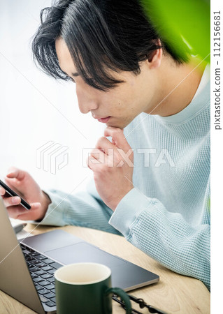 Young man working on a computer in the living room Young man working on a computer in the living room 112156681