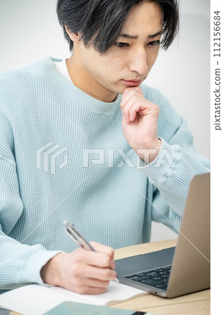 Young man working on a computer in the living room Young man working on a computer in the living room 112156684