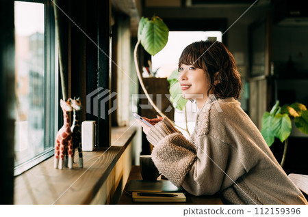 窗邊櫃檯上微笑的女士使用智慧型手機 窗邊櫃檯上微笑的女士使用智慧型手機 112159396
