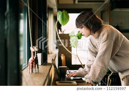 一位女士在靠窗的櫃檯上使用電腦 一位女士在靠窗的櫃檯上使用電腦 112159397