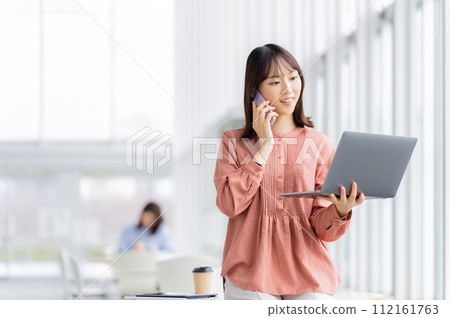 Business woman talking on smartphone while looking at computer Business woman talking on smartphone while looking at computer 112161763