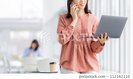 Business woman talking on smartphone while looking at computer 112162110