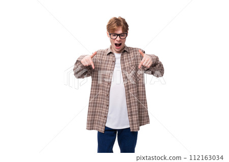 handsome red-haired caucasian student guy in glasses dressed in a plaid shirt joyfully shows his handsome red-haired caucasian student guy in glasses dressed in a plaid shirt joyfully shows his 112163034