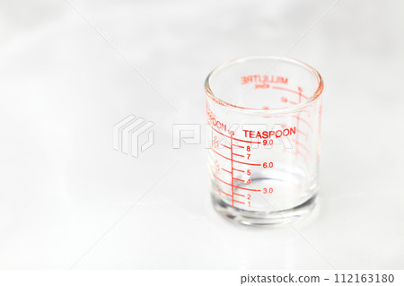 glass measuring cup or dosage cup with teaspoon measurements displayed. glass measuring cup or dosage cup with teaspoon measurements displayed. 112163180