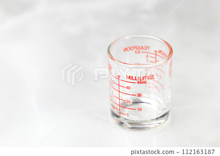glass measuring cup or dosage cup with millilitre measurements displayed. 112163187
