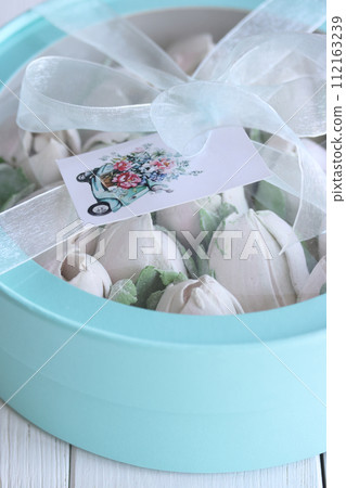 Zephyr in a box. Marshmallow tulips. The box is turquoise in color, tied with a ribbon. It stands on white boards. Taken from above. Close-up. Zephyr in a box. Marshmallow tulips. The box is turquoise in color, tied with a ribbon. It stands on white boards. Taken from above. Close-up. 112163239
