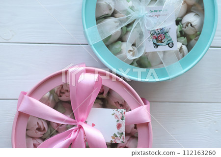 Zephyr in boxes. Marshmallow tulips. The boxes are turquoise and pink, tied with ribbon. On white boards. Taken from above. 112163260