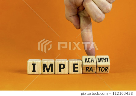 Imperator or impeachment symbol. Businessman hand turns wooden cubes and changes the word 'imperator' to 'impeachment'. Beautiful orange background, copy space. Business, impeachment concept. 112163438
