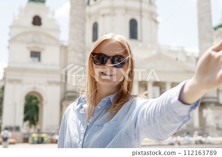 Photo relaxed charming positive young woman hold camera and make selfie summer outside in city center outdoors. Lifestyle tourist travel holiday concept. Point of view. St. Charles's Church, Vienna Photo relaxed charming positive young woman hold camera and make selfie summer outside in city center outdoors. Lifestyle tourist travel holiday concept. Point of view. St. Charles's Church, Vienna 112163789