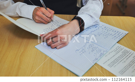 A girl student writes math formulas in a notebook. Notebook close-up. 112164115