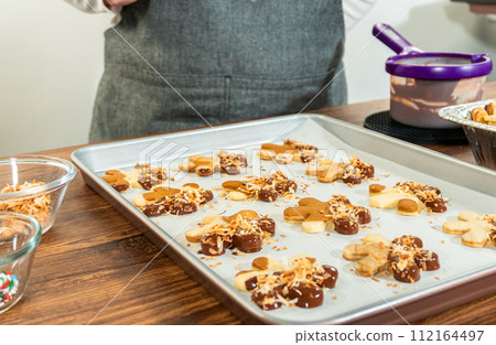 Gingerbread men cookies, chocolate-dipped feet, generously sprinkled with golden toasted coconut shavings, artfully arranged on parchment paper. 112164497