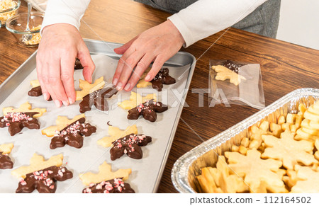 Preparing star-shaped cookies, half-dipped in chocolate, accented with peppermint chocolate chips for the holidays. Preparing star-shaped cookies, half-dipped in chocolate, accented with peppermint chocolate chips for the holidays. 112164502