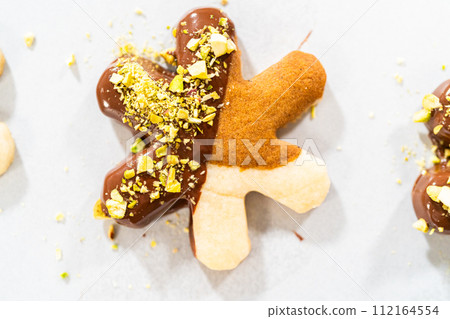 Crafting star-shaped holiday cookies dipped in chocolate and sprinkled with crushed pistachios, arranged on parchment paper. 112164554