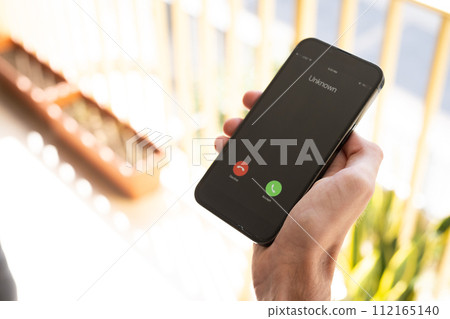 Fraud or fraudulent schemes. Close-up of a male hand holding a phone with an unexpected incoming call from an unknown 112165140